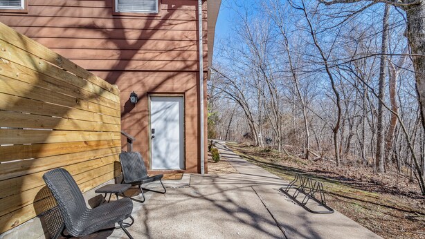 A patio with two chairs and a table, a wooden fence, and a building with a door and windows. - Private Suite, Sleep and Bike- Seconds 2  trail! Private Basement Apartment. (Bella Vista)