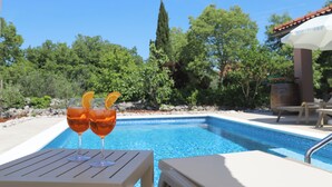 Ein Poolbereich mit zwei Gläsern mit Getränken, einer Liege und einer Pergola mit einem weißen Sonnenschirm.