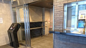 A reception area with a digital kiosk, a glass door entrance, and a computer monitor displaying a welcome message. - ESLEAD HOTEL Namba South 2 (Osaka)