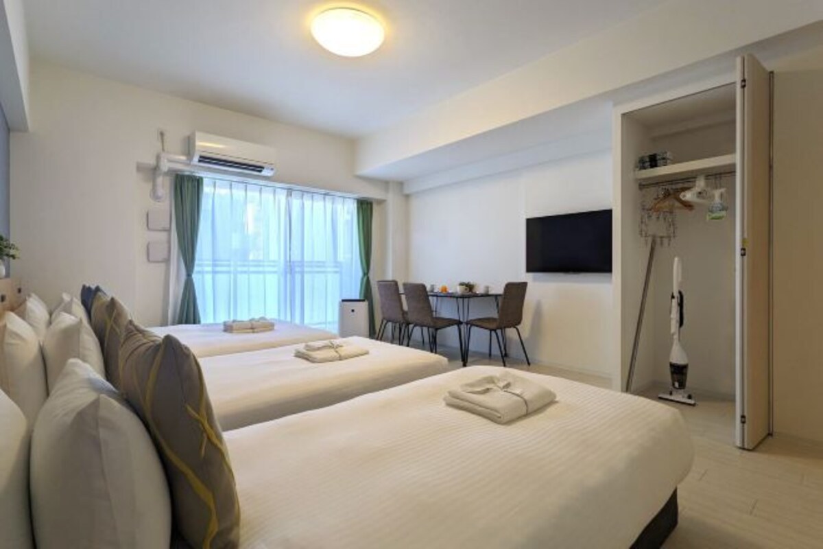 A hotel room with two beds, a dining table with chairs, a TV mounted on the wall, and an open closet.