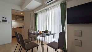 A dining area with a table set for four, chairs, a TV mounted on the wall, and an air conditioning unit above the window. - ESLEAD HOTEL Namba South 2 (Osaka)