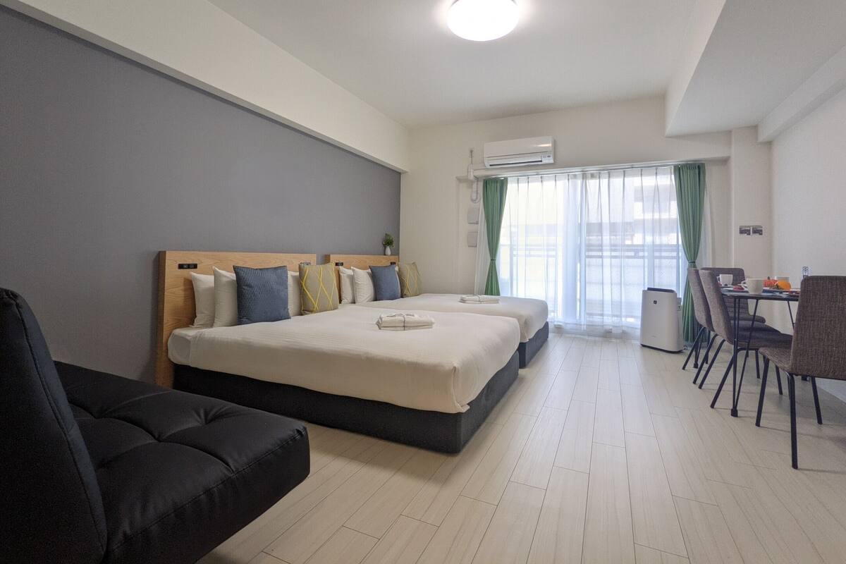 Ein Hotelzimmer mit zwei Betten, einem Sofa, einem Esstisch mit Stühlen und einem Fenster mit Vorhängen.