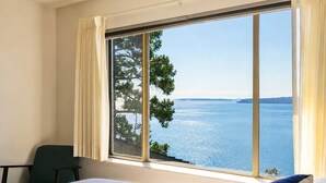 A hotel room with a large window offering a view of the sea and trees. - SaliHaven: Oceanfront 3 BR 3 Beds 3.5 Ba + Gym (Pender Island)