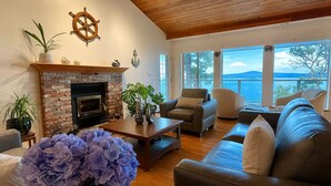 A living room with a fireplace, a sofa, a coffee table, and a view of the sea. - SaliHaven: Oceanfront 3 BR 3 Beds 3.5 Ba + Gym (Pender Island)