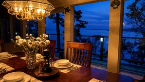 A dining table set with plates, bowls, cutlery, a vase with flowers, and a table lamp. - SaliHaven: Oceanfront 3 BR 3 Beds 3.5 Ba + Gym (Pender Island)