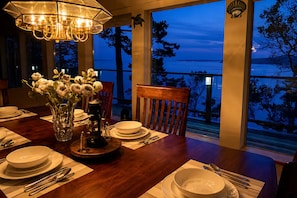 A dining table set with plates, bowls, cutlery, a vase with flowers, and a table lamp.