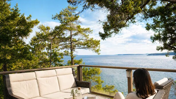 A deck with a sofa and chairs, a table with a tray, and a view of the water. - SaliHaven: Oceanfront 3 BR 3 Beds 3.5 Ba + Gym (Pender Island)