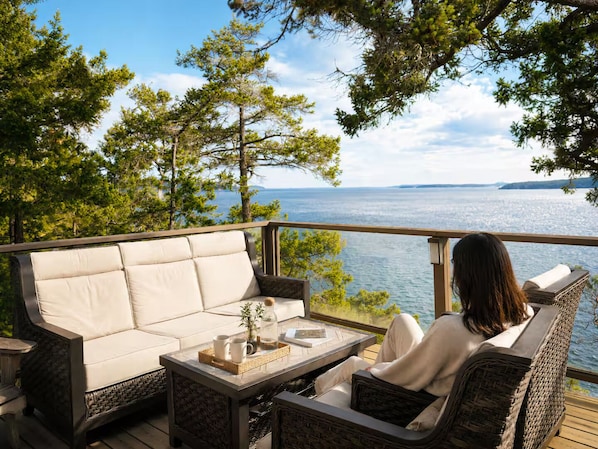 A deck with a sofa and chairs, a table with a tray, and a view of the water.