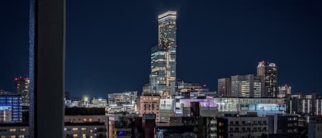 Une vue nocturne d’une ville, avec un gratte-ciel imposant dont le design original présente une forme torsadée.