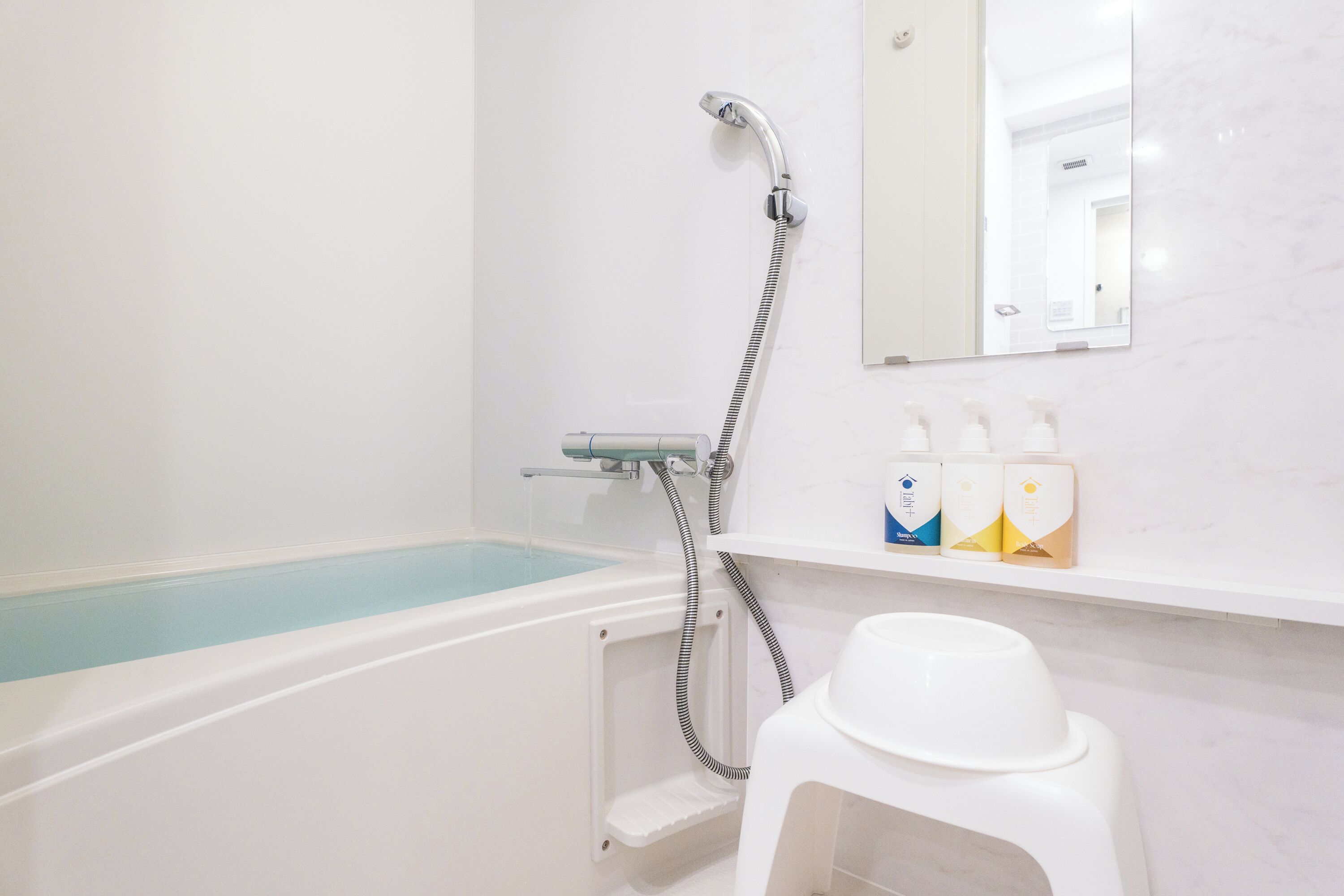 Een badkamer met een bad, douche en toilet. Toiletartikelen staan op de plank.