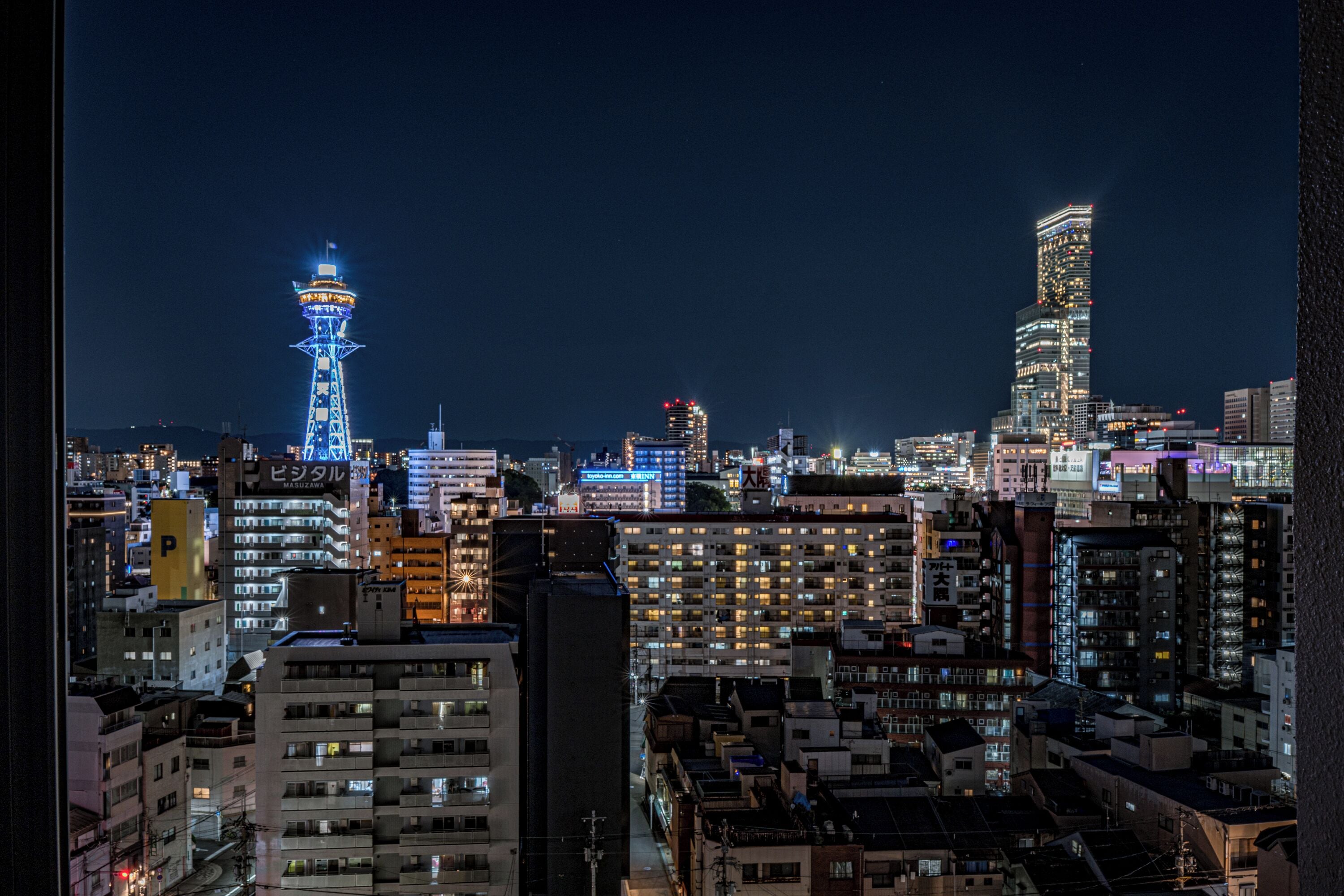Een stadsgezicht 's nachts met verlichte gebouwen, waaronder een toren en een hoog kantoorgebouw.