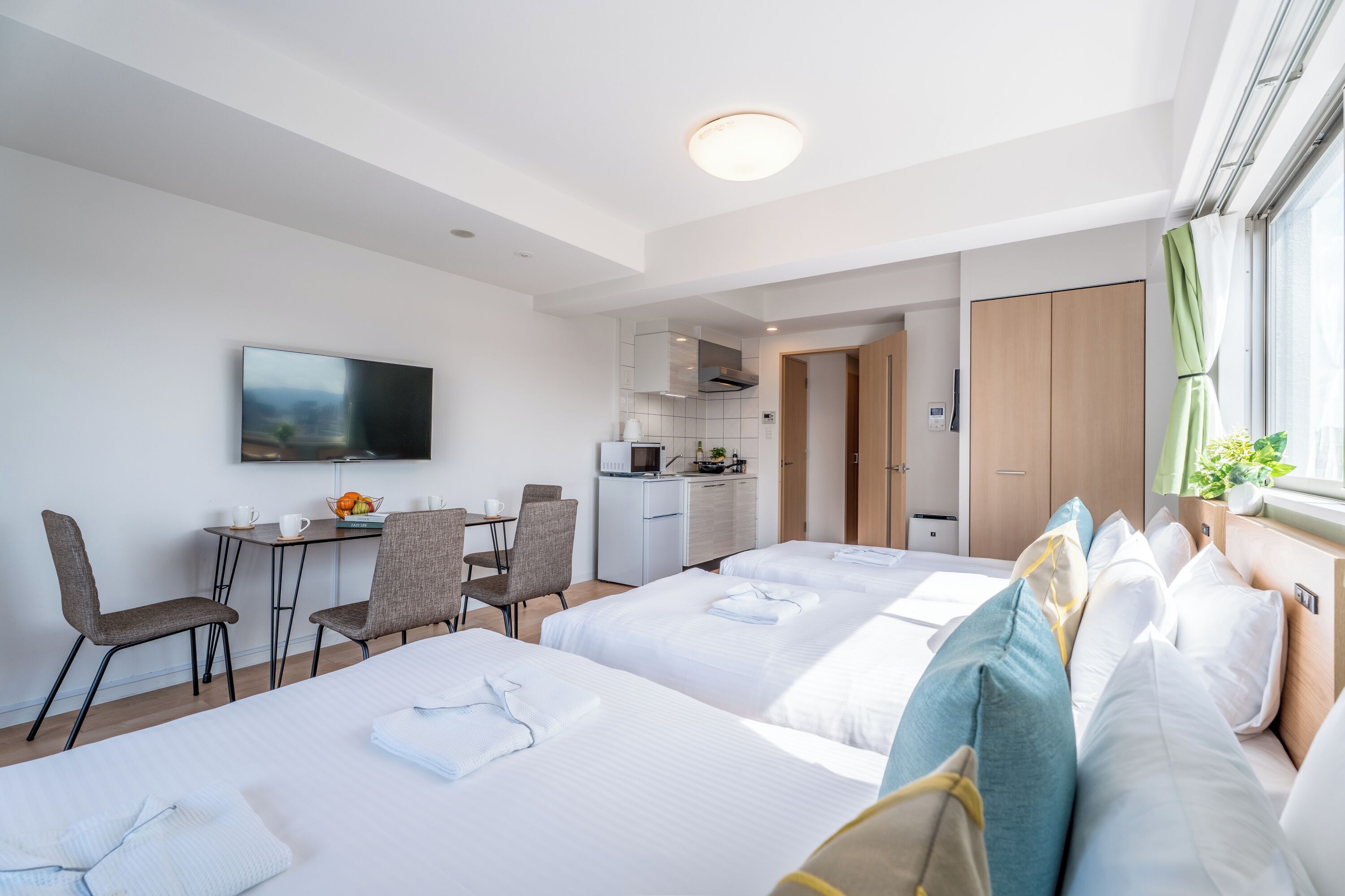 A hotel room with two beds, a desk with chairs, a television, and a kitchenette.