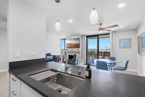 A modern kitchen with a large island, a dining area with blue chairs, and a view of the city through large windows.