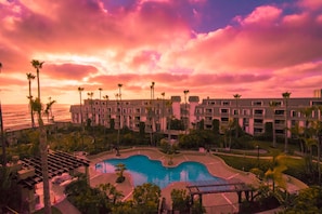 Ein Resort mit Pool, Palmen und Blick auf den Ozean bei Sonnenuntergang.
