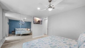 A bedroom with a bed, a ceiling fan, a large mirror, and a wall-mounted picture.