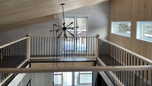 A spacious loft with a high ceiling, exposed wooden beams, a central hanging light fixture, and large windows offering views of the outdoors. - Oasis thermal -  Mauricie- N.E. Chic Shack (Saint-Mathieu-du-Parc)
