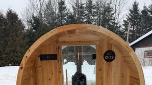 A wooden sauna with two benches and a glass door, set on a snowy ground with trees in the background. - Oasis thermal -  Mauricie- N.E. Chic Shack (Saint-Mathieu-du-Parc)