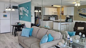 A living room with a beige sofa, a dining table with chairs, a kitchen area with white cabinets, and a ceiling fan. - BEACH & POOL VIEW!! LOCATED DIRECTLY ON THE BEACH!! (Panama City Beach)