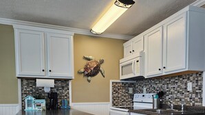 A kitchen with white cabinetry, a central island with stools, a microwave, and a stove. - BEACH & POOL VIEW!! LOCATED DIRECTLY ON THE BEACH!! (Panama City Beach)