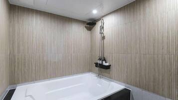 A modern bathroom with a large bathtub, a shower, and a small shelf with toiletries.