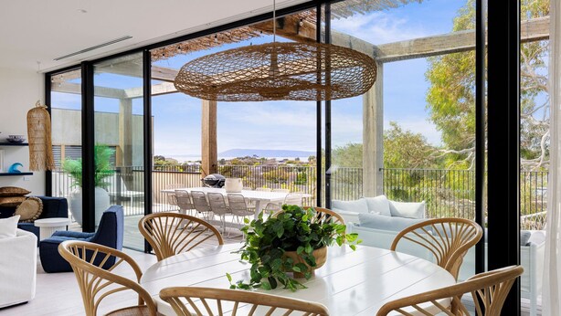 A modern dining area with a large window overlooking a scenic view, a hanging woven light fixture, and a dining table surrounded by chairs.