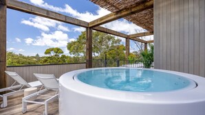 A hot tub with lounge chairs on a wooden deck, surrounded by a wooden fence and trees.