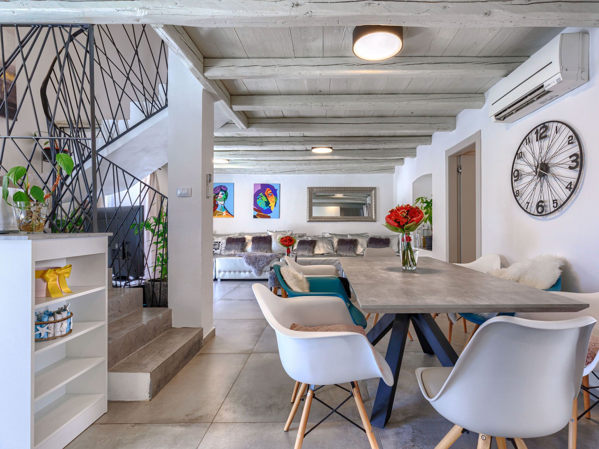 A modern dining area with a long table, white chairs, and a decorative clock on the wall.
