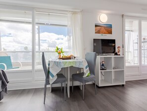 A modern living room with a dining area, large windows with a view of the sky, a flat-screen TV, and a small shelf with a figurine. - Les Marinas by Interhome (Courseulles)