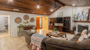 Een ruime woonkamer met een hoge plafond, houten balken, een open haard en een gezellige zithoek met een gebreid plaid.