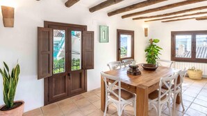 A dining area with a wooden table, white chairs, and a potted plant. - Magnificent rustic house with pool, garden, and views (Acequias)