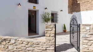 A stone-walled building with a white facade, a metal gate, and a potted plant. - Magnificent rustic house with pool, garden, and views (Acequias)