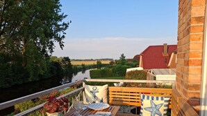 Eine Holzterrasse mit einem Tisch für zwei Personen, mit Blick auf einen Fluss und Grünflächen.