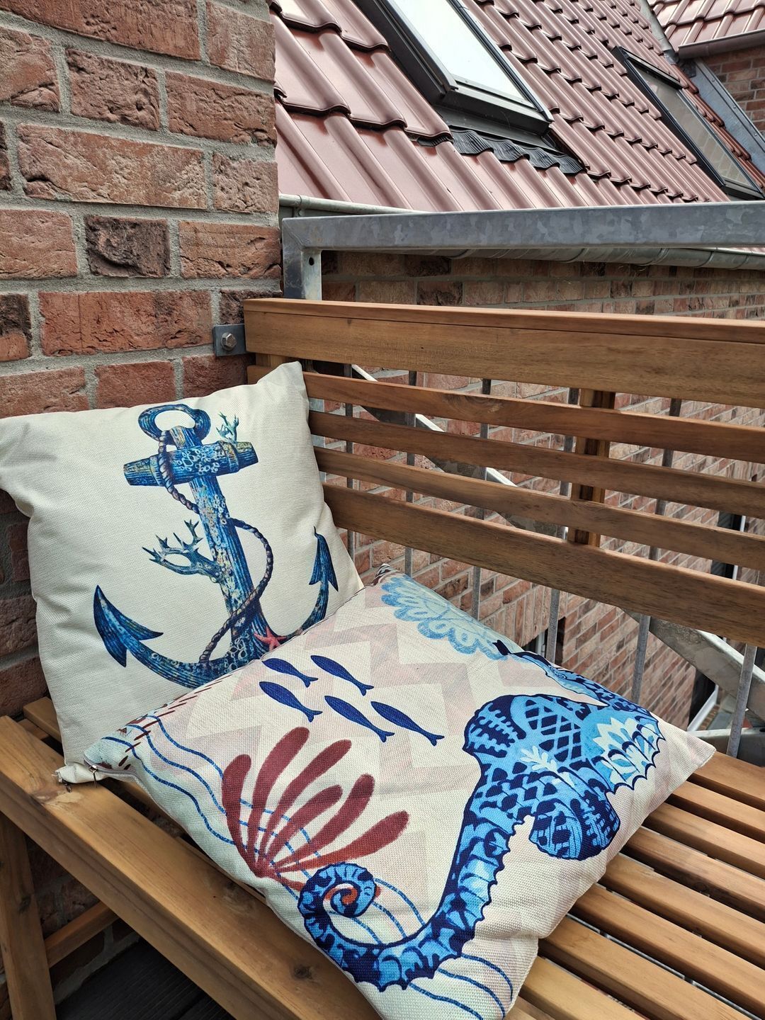 A wooden bench with a cushion featuring a blue anchor and fish design.