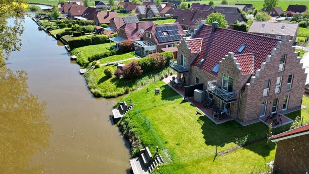 Ein Wohngebiet mit Häusern entlang eines Kanals, mit Backsteingebäuden, grünen Rasenflächen und blauem Himmel.