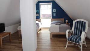Ein Schlafzimmer mit schrägen Wänden, einem Bett, einem Sessel und einem Fernseher auf einem Schrank.