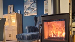 Ein Zimmer mit Kaminofen, blauer Wand, einer Schrank mit Glastüren und einem Streifenstuhl.