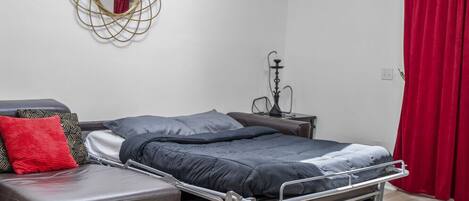 A modern bedroom with a metal bed frame, a grey sofa, and a red curtain.