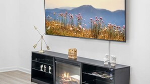 Un salon moderne avec un téléviseur à écran plat fixé au mur, un meuble de rangement noir avec des étagères et une cheminée.