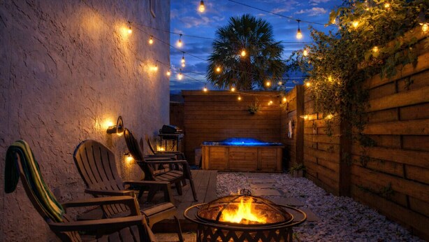 Une terrasse extérieure avec un foyer, des chaises en bois, des guirlandes lumineuses et un mur en bois.