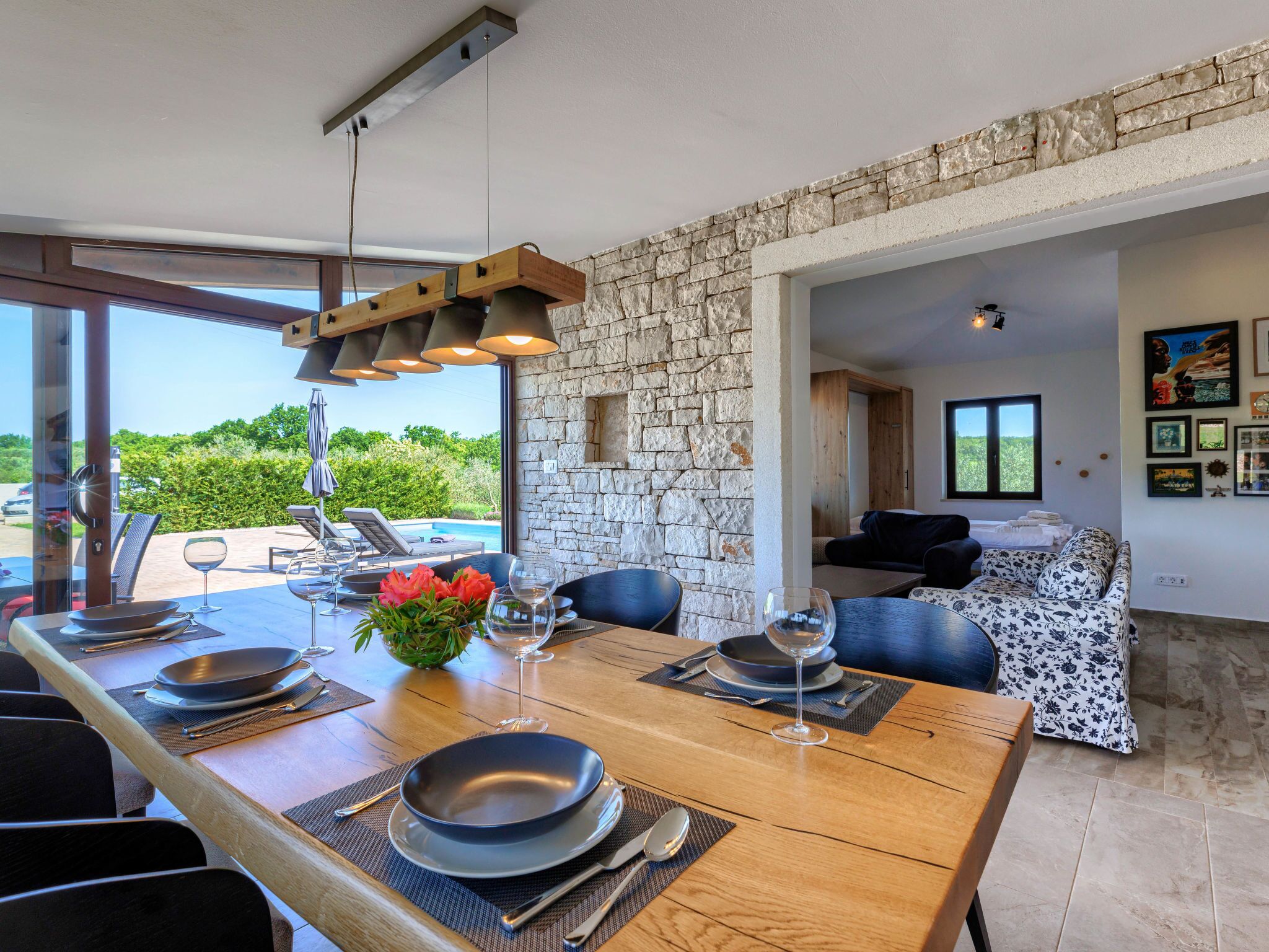 A dining area with a stone wall, a pool view, and a living area with a sofa and artwork.