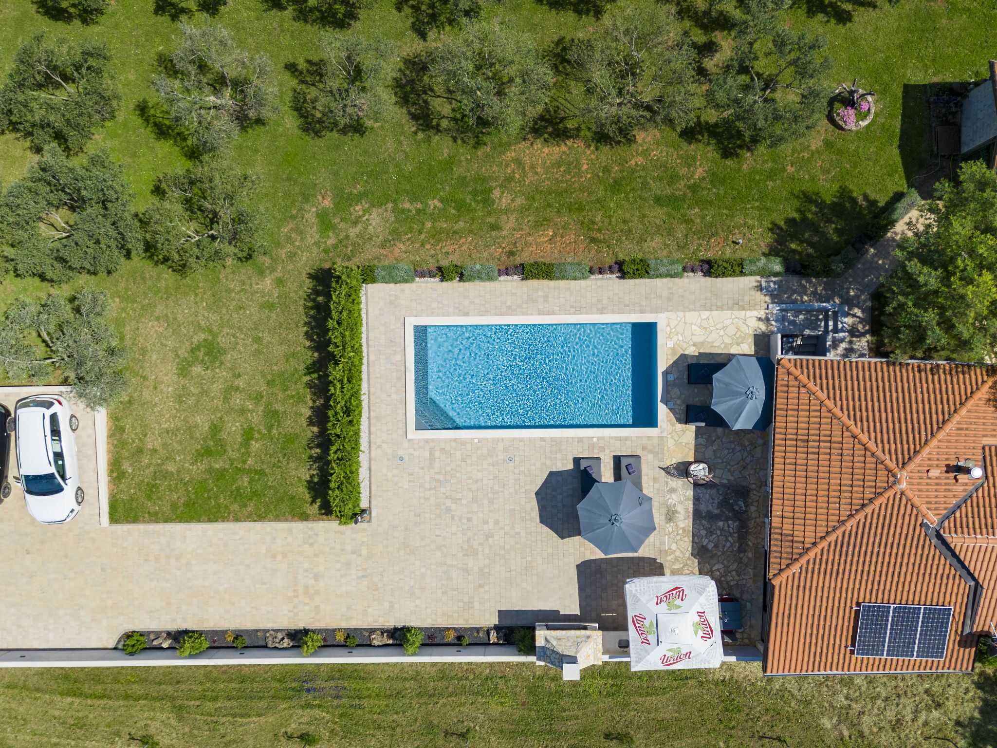 An aerial view of a property with a swimming pool, patio furniture, and a car parked nearby.