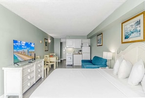 A hotel room with a bed, a TV, a kitchenette, and a dining area.