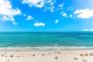 A beach with clear blue water, a sandy shore, and a few umbrellas. - Sea Mist 21004 (Myrtle Beach)