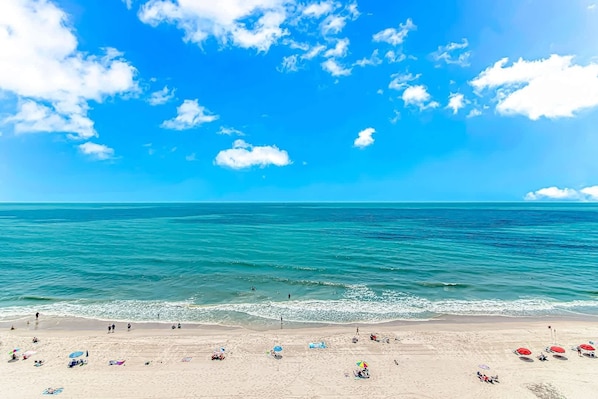 A beach with clear blue water, a sandy shore, and a few umbrellas.