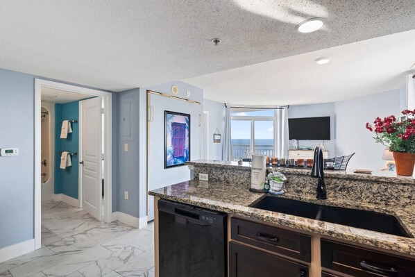 A modern kitchen with granite countertops, a dishwasher, and a view of the ocean.