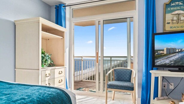 A room with a bed, a TV, a chair, a wardrobe, and a balcony with a view of the sea. - Bay Watch 1441 (North Myrtle Beach)