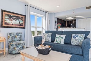 A living room with a blue sofa, a chair, a table, and a framed picture on the wall.