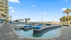 A swimming pool area with multiple water slides, a brick walkway, and a palm tree in the background. - Bay Watch 1441 (North Myrtle Beach)