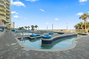 A swimming pool area with multiple water slides, a brick walkway, and a palm tree in the background.