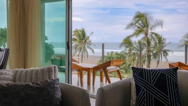 Una habitación con vistas a la playa, un sofá, una mesita de centro y una ventana con cortinas.